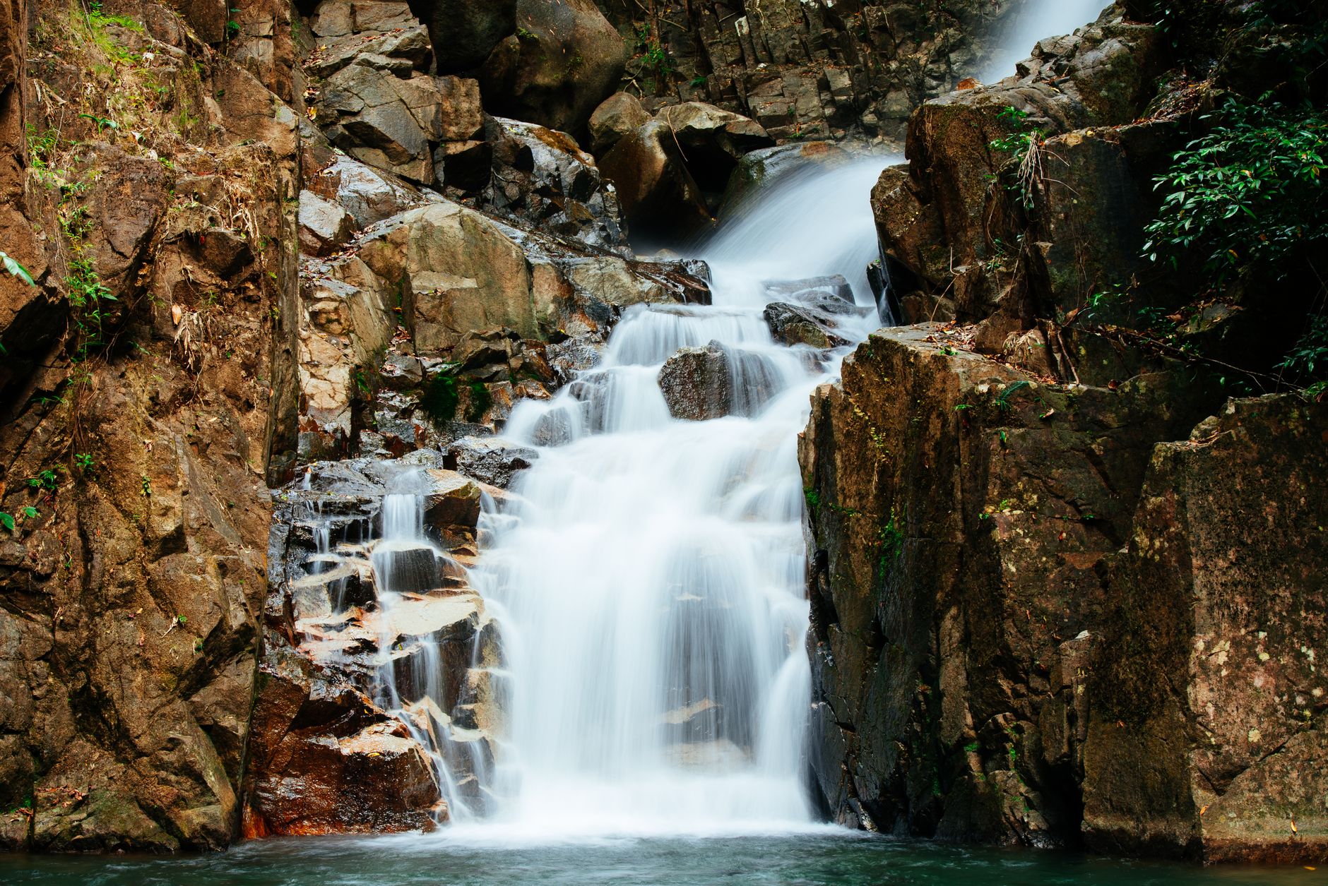 Waterfall cascading over rocky cliffs into a clear pool in Khao Yai National Park, surrounded by lush greenery