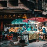 Colorful Thai night market with street food stalls, umbrellas, and vendors at night in an urban setting