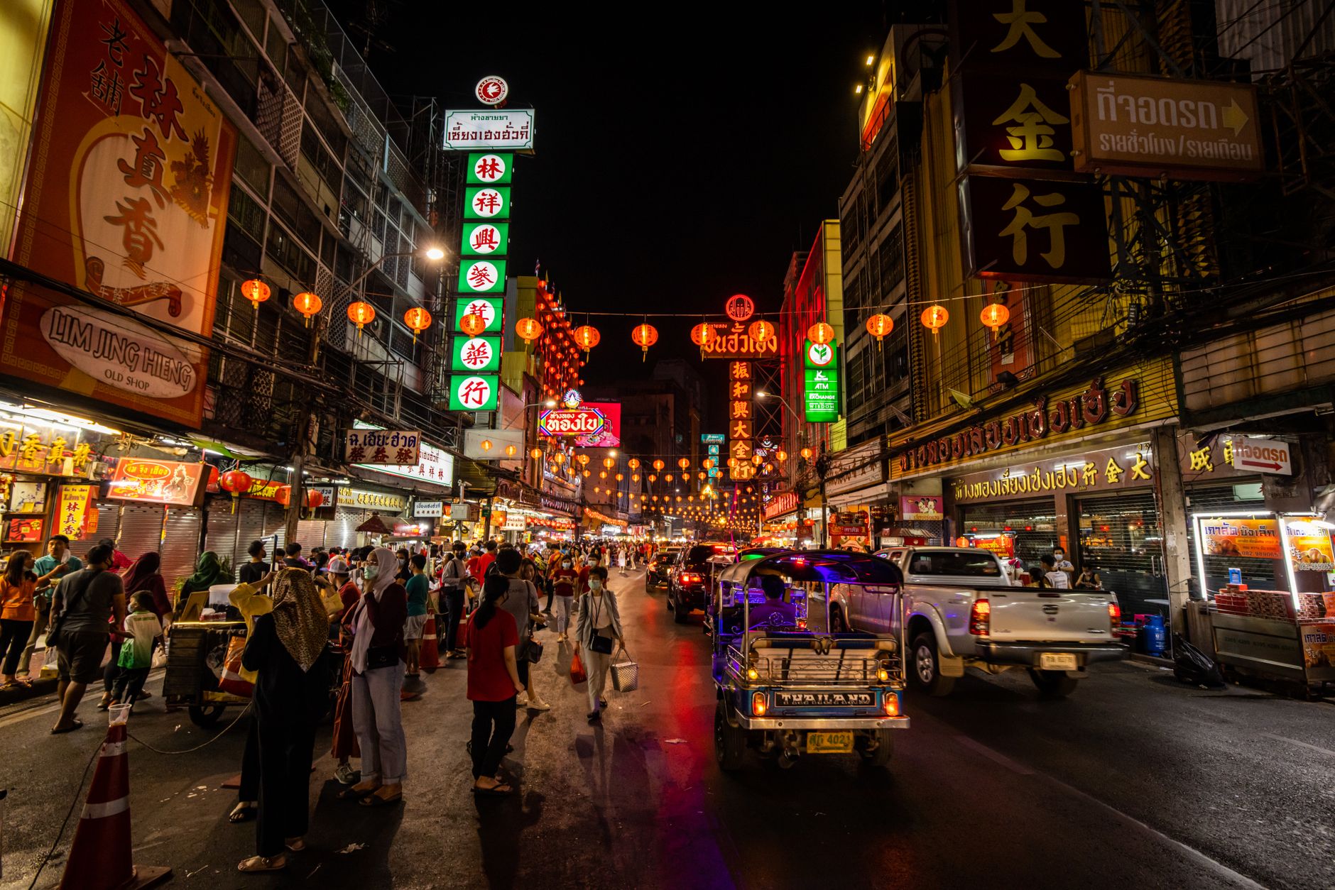 Vibrant Thai night market street with neon signs, busy traffic, and bustling city atmosphere
